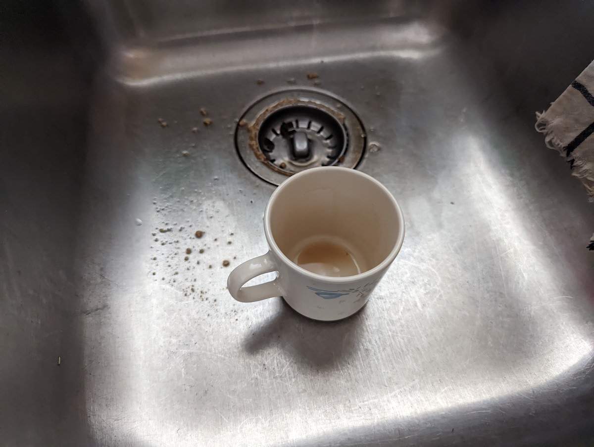 close up of a dirty mug in a dirty metal sink